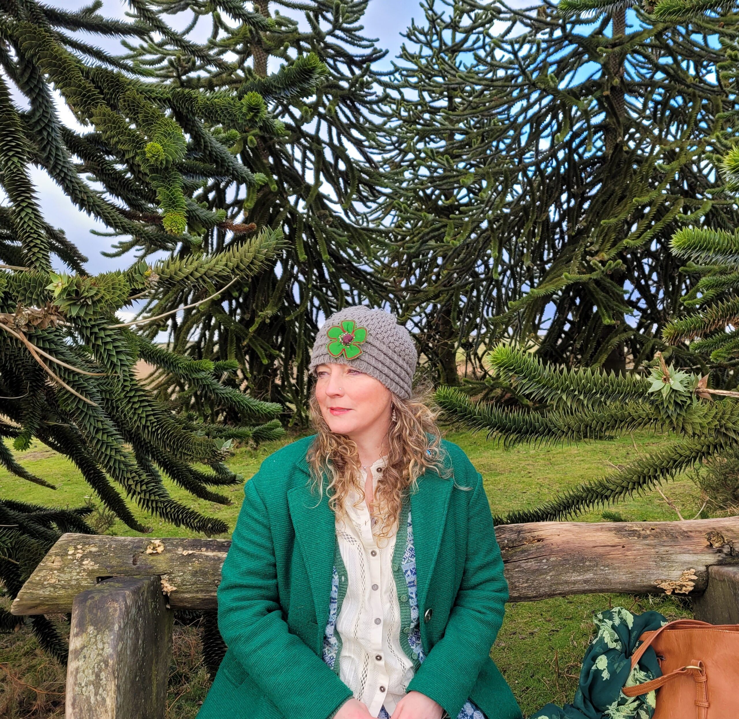 Photograph of a blonde woman, wearing a green cardigan with trees in the background