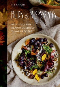 A book cover. Liz Knight Buds & Blossoms Delicious and Beautiful edible flower recipes. There is a plate on the bottom half of the cover with a colourful salad style dish. The plate is resting on a earth toned piece of material, on top of a table. 
