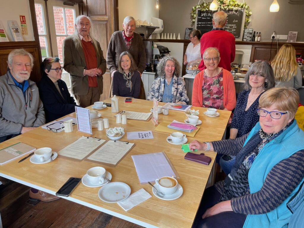 A colour photograph of a group of people sat around a table in a cafe.